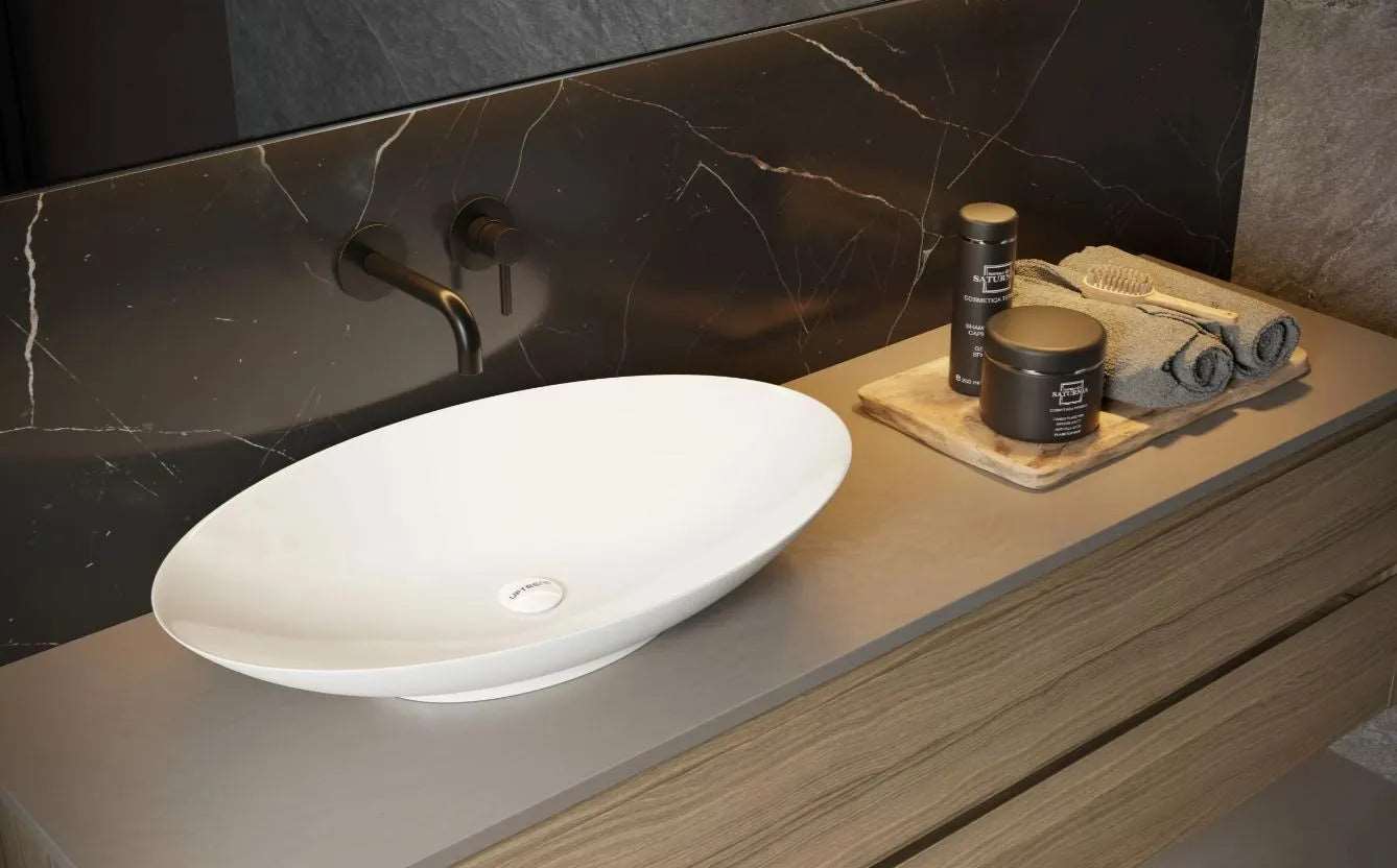 Witte ovale keramische waskom 42x67,5x12 cm op modern badmeubel met zwarte wandkraan en donkere marmeren achterwand in luxe badkamer