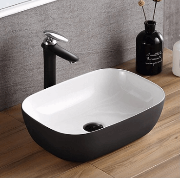 Witte rechthoekige keramische waskom 45,5x32x13,5 cm met matzwarte buitenzijde op houten badmeubel, gecombineerd met zwarte opbouwkraan en grijze wand.