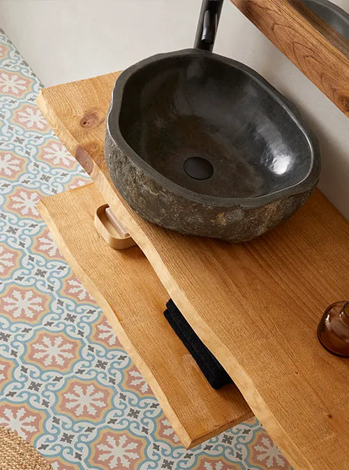 Natuurstenen opbouwwaskom 45x40x15cm in organische ovale vorm op warm houten blad, gecombineerd met zwarte kraan, handdoek en accessoires voor een moderne badkamerstijl.