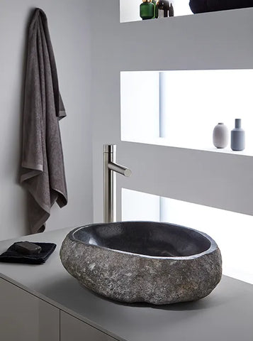 Grijze organische riviersteen waskom 45x40x15cm met donkere gepolijste binnenzijde op licht badmeubel met RVS-opbouwkraan in minimalistische badkamer.