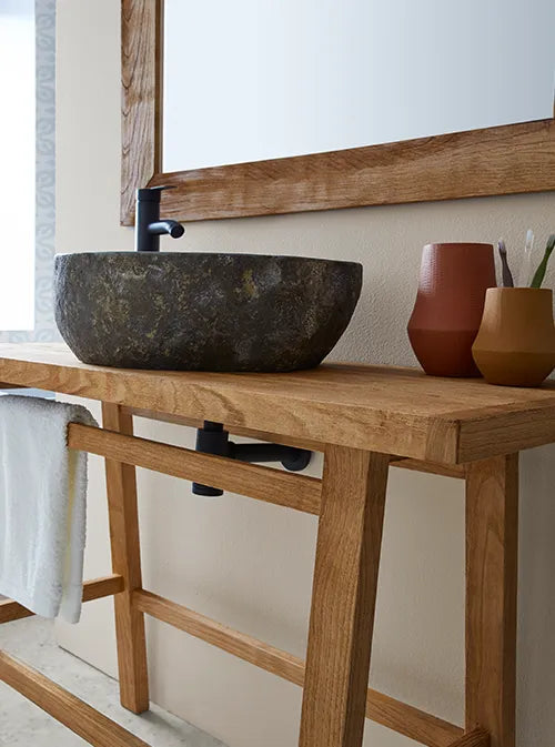 Natuurstenen opbouwwaskom 45x40x15cm in organische ovale vorm op warm houten blad, gecombineerd met zwarte kraan, handdoek en accessoires voor een moderne badkamerstijl.