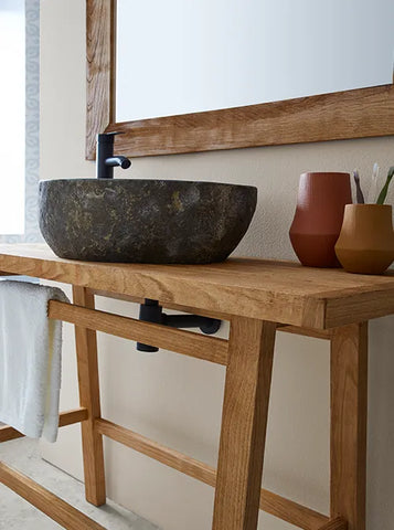 Natuurstenen opbouwwaskom 45x40x15cm in organische ovale vorm op warm houten blad, gecombineerd met zwarte kraan, handdoek en accessoires voor een moderne badkamerstijl.