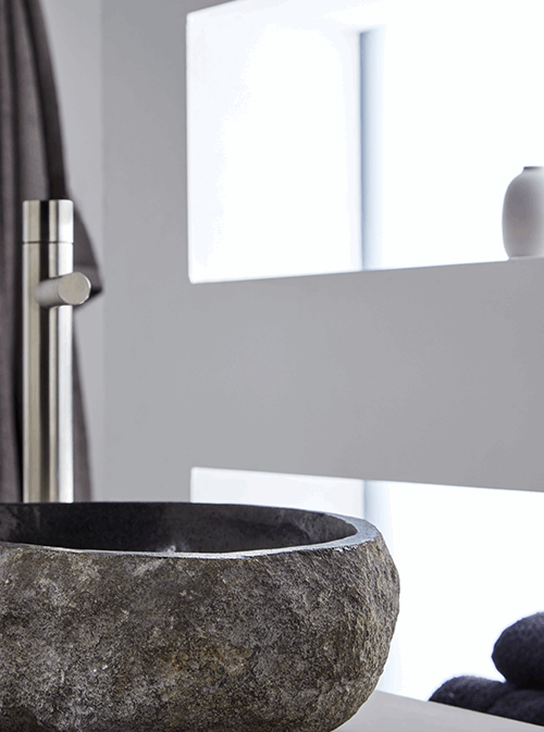 Close-up van ronde grijze riviersteen waskom 45x40x15cm met gepolijste rand en binnenzijde, gecombineerd met rvs opbouwkraan in moderne badkamer.