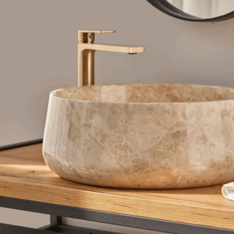 Ronde beige natuurstenen waskom 40x40x15 met subtiele travertinlook en centrale afvoeropening op houten badmeubel met gouden kraan