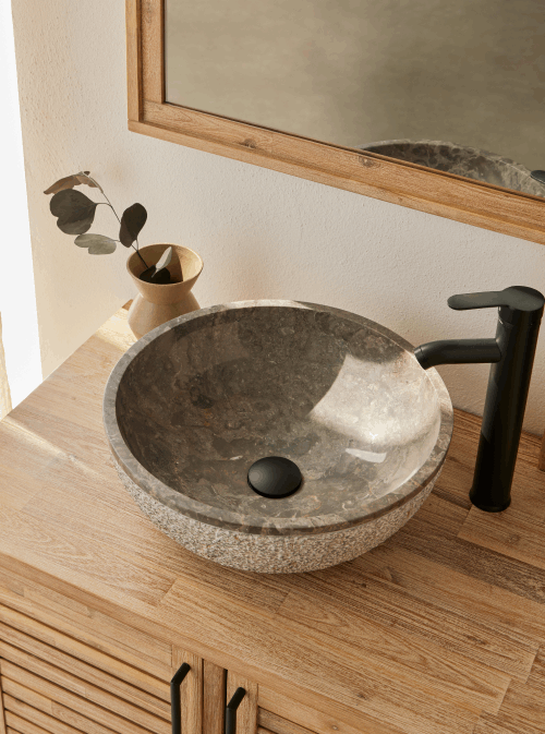 Ronde grijze natuurstenen waskom 40x40x15cm met gepolijste binnenzijde en gehamerde buitenkant op houten badmeubel met zwarte opbouwkraan.