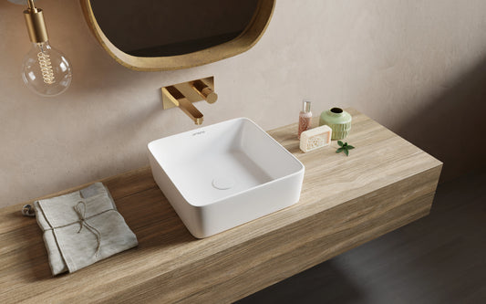 Witte keramische waskom met vierkante vorm op houten badkamermeubel met gouden wandkraan